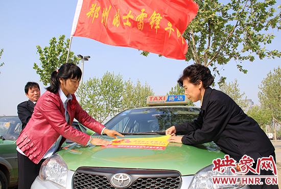 　　授旗結(jié)束后，首都的士雷鋒車隊王鳳進隊長（右）與鄭州的的哥的姐在車身上貼上標識。