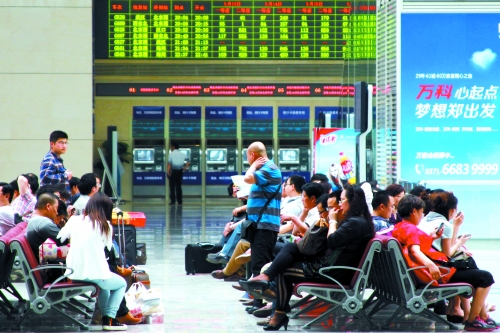 候車大廳溫度很高，一名乘客一手扇風(fēng)、一手擦汗