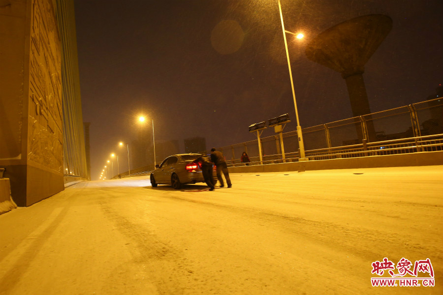 雪天路滑，汽車上橋打滑，兩名“推車人”幫助一輛私家車上坡。