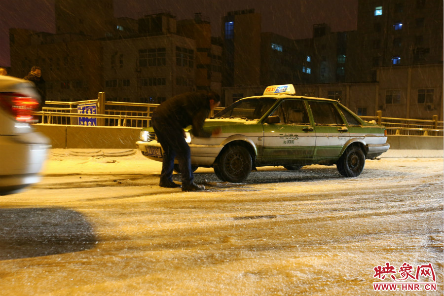 一位出租車司機在車輪前灑上雪，希望能增加輪胎的摩擦力。