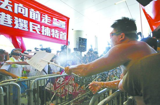 17日，在香港立法會(huì)外，一名反對政改的男子向支持派人群投擲標(biāo)牌。