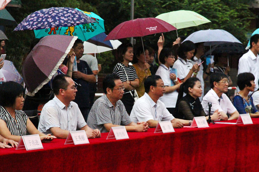 在主席臺上觀看的校領(lǐng)導(dǎo)也堅持不打傘陪學生一起淋雨，身旁站滿了打傘觀看的家長。